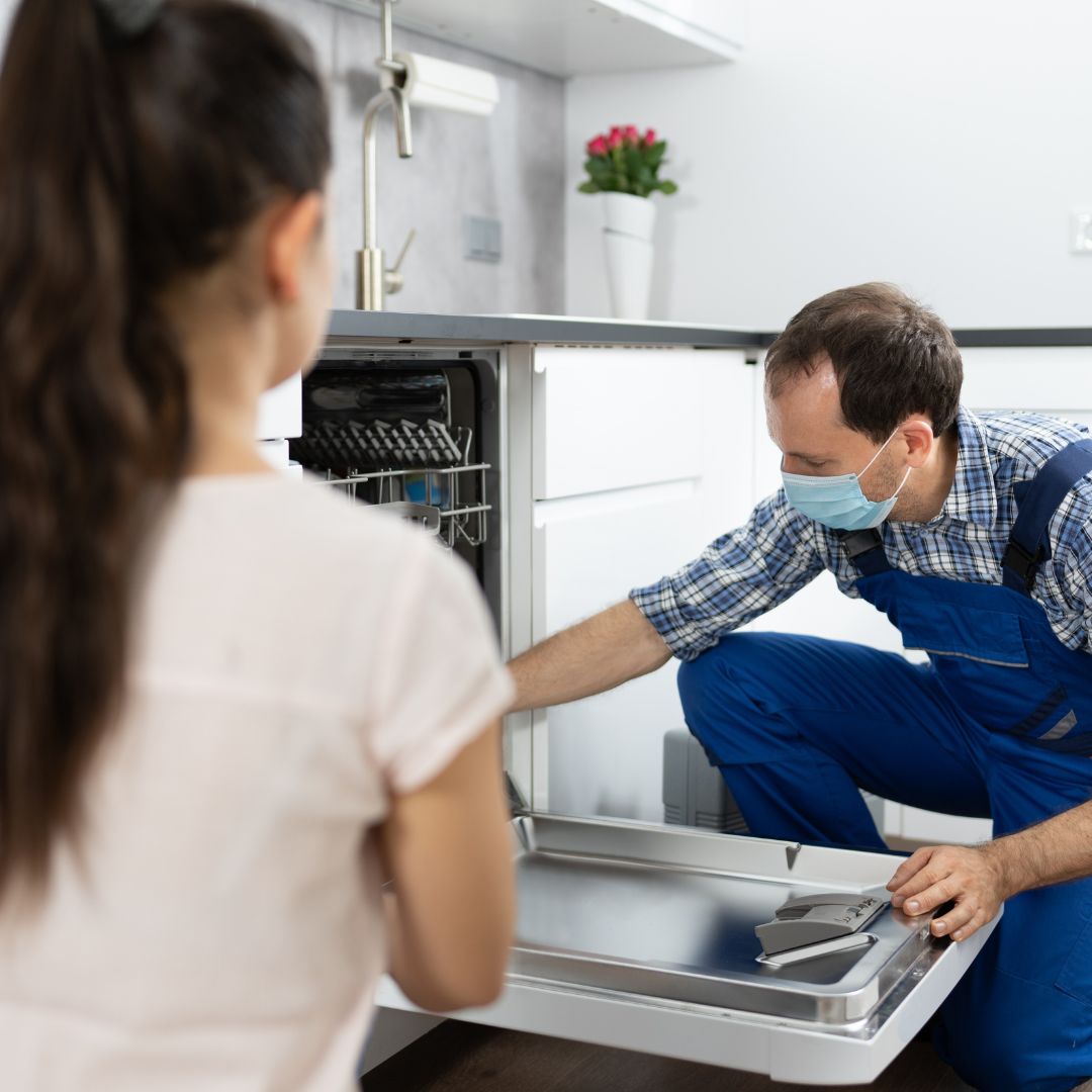 plumber repairing dishwasher while client watches plumber repairing dishwasher while client watches